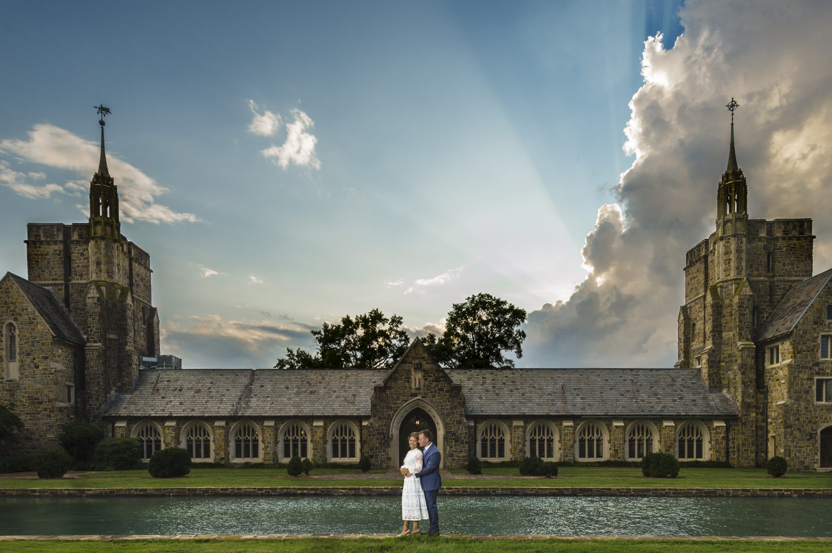 couple snuggle in front of historic building sun flare and storm clouds