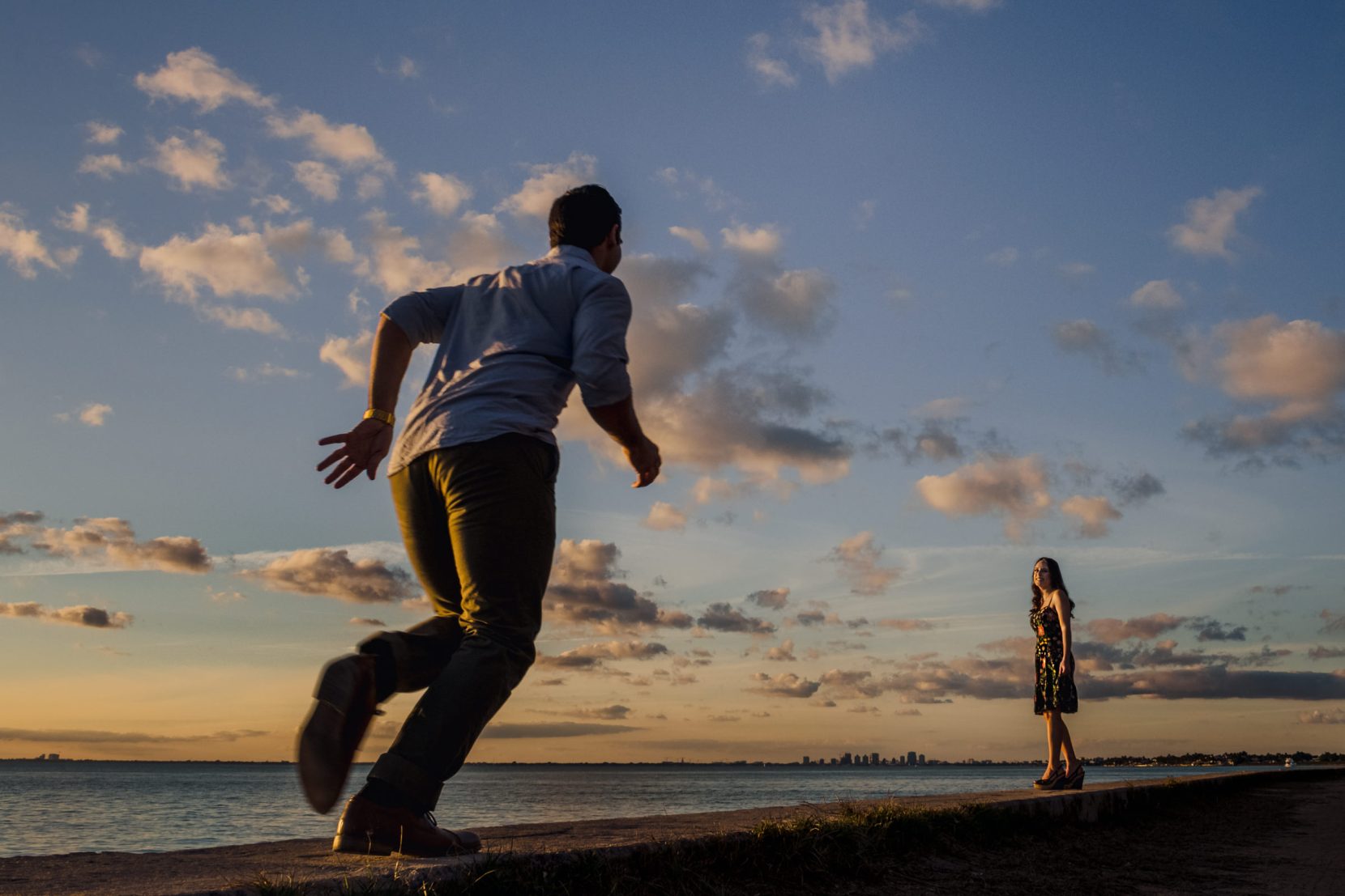 man running to girl along beach in miami during sunset clouds city