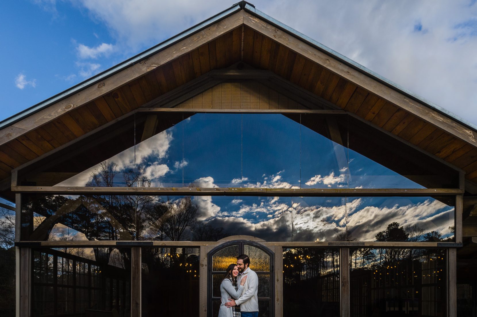 couple hug in front of glass building cloud reflection
