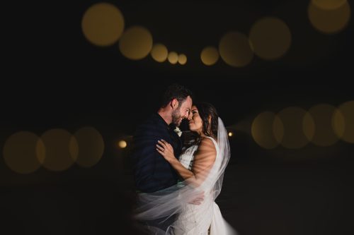bride and groom hugging with veil blowing bokeh cafe lights