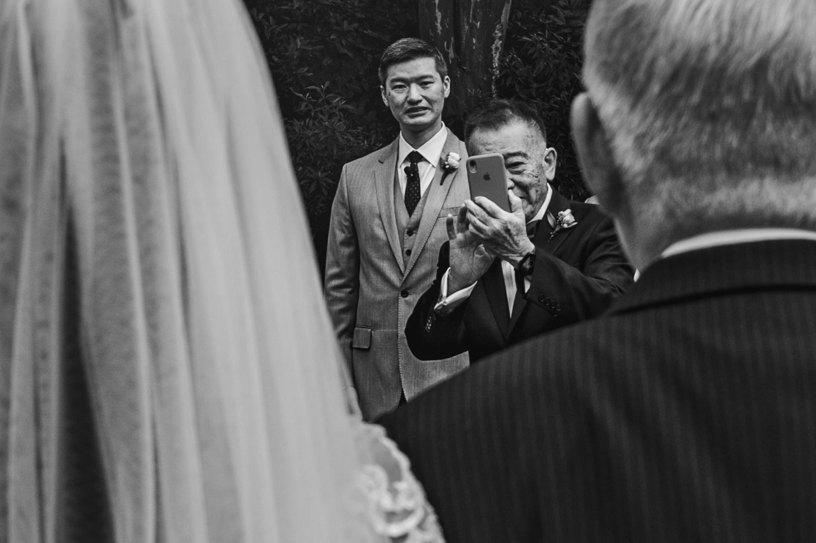 father of groom takes cell phone photo during wedding processional
